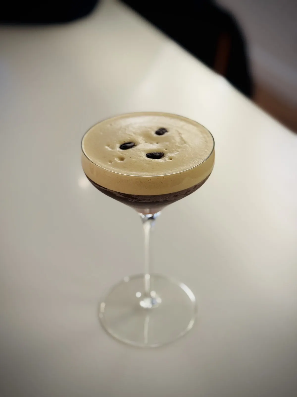 An Espresso Martini with tan coffee foam and coffee-bean garnish