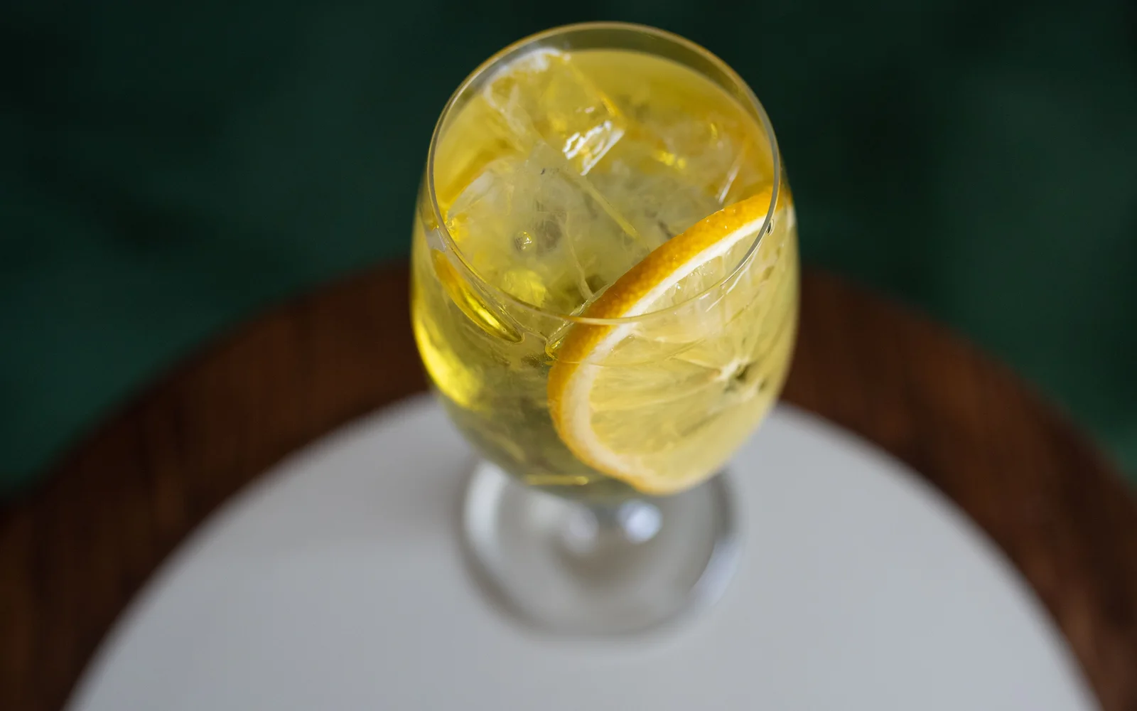 A pale yellow sparkling long drink with ice and lemon in a stemmed glass