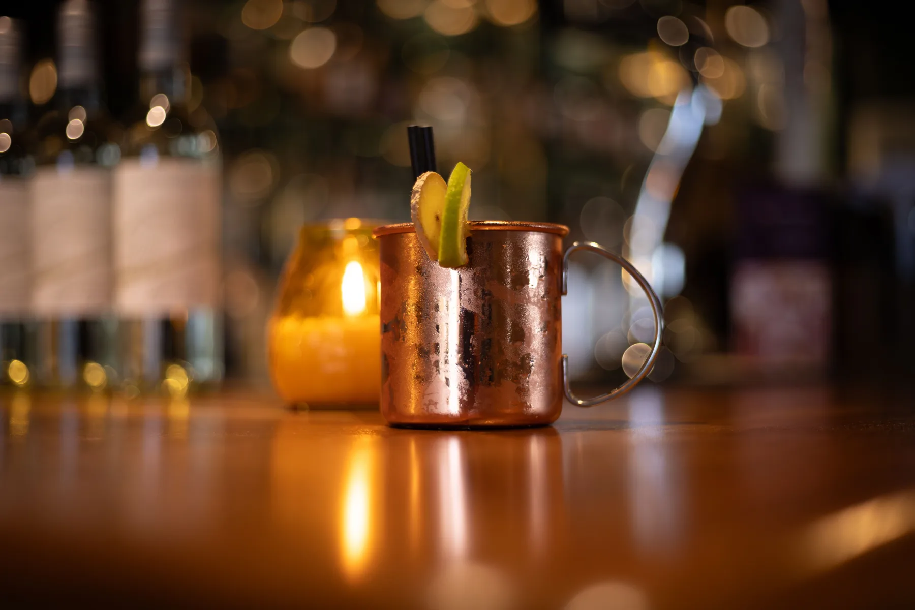 An iced copper-colored mug garnished with lime and a slice of ginger on a warmly lit bar