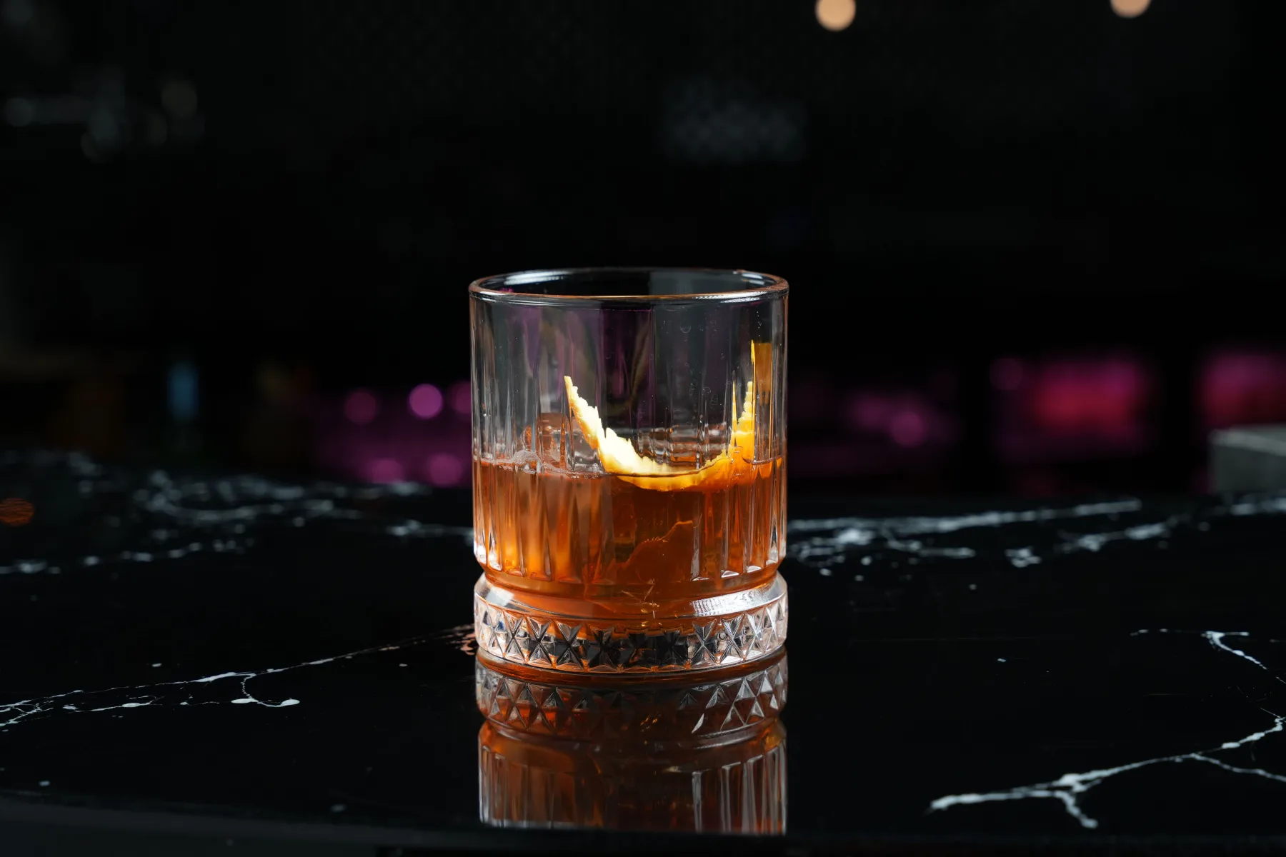 黑色吧台上一杯琥珀色 Old Fashioned，以橙皮装饰