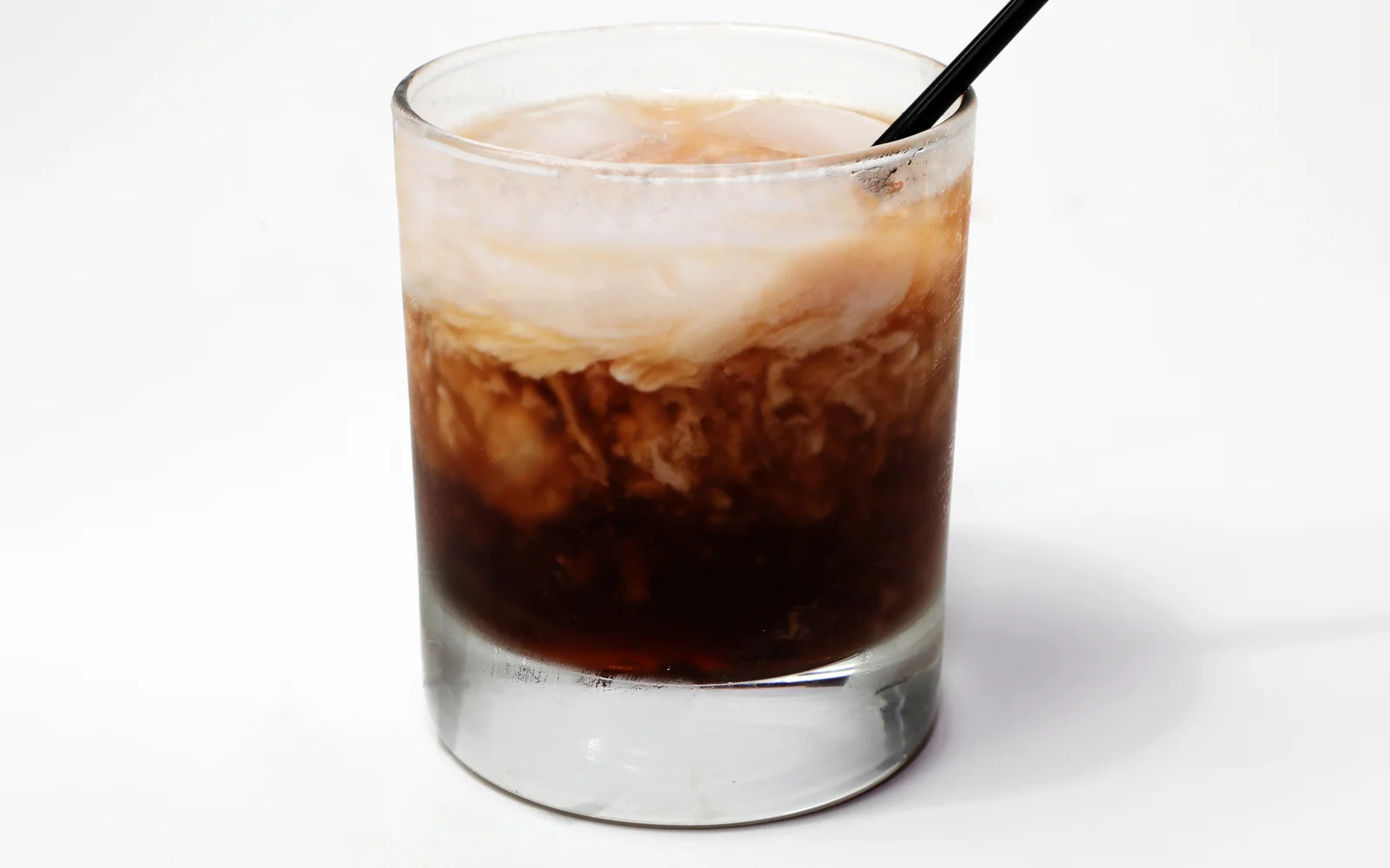 A White Russian in a short rocks glass over large ice, with pale cream marbling into a dark coffee-colored base